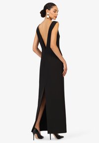 Robe noire longue jusqu'au sol avec un dos plongeant, un design ajusté et une fente sur le côté. Dispose de larges bretelles et d'une texture lisse.