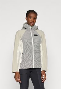Veste légère zippée en beige et gris, avec une capuche texturée, des accents de couture diagonale et deux poches zippées latérales.