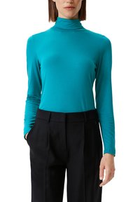 Turkusowa bluzka z długim rękawem i golfem, wykonana z miękkiego materiału, o dopasowanym kroju, bezszwowym dekolcie, zestawiona z czarnymi spodniami o wysokim stanie.