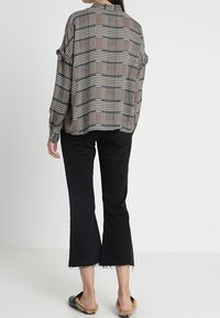 Blusa a maniche lunghe a quadri in toni neutri con vestibilità rilassata, abbinata a jeans neri a vita alta e svasati, e scarpe slip-on pelose.
