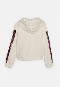 Krämsfärgad kort hoodie med dragsko i huvan, med iögonfallande rosa och svarta leopardmönster längs ärmarna. Mjuk tygtextur.