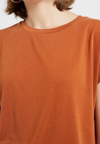Rust orange T-shirt with short sleeves, round neckline, and soft, textured fabric. Simple, relaxed fit without visible patterns or accents.