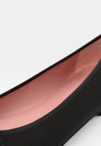 Bailarina preta com um exterior suave, apresentando um interior rosa claro. O sapato tem uma borda fina e um design minimalista.