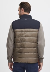 Gepolsterte Weste mit einem khakifarbenen unteren Abschnitt und einem marineblauen oberen Teil. Sie verfügt über einen hohen Kragen und gerippte Ärmel und zeigt eine gesteppte Textur.