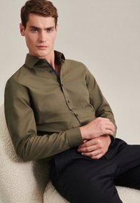 Olijfgroene overhemd met lange mouwen, een button-down kraag, knopen aan de voorkant en een patroon aan de binnenkant van de kraag, gecombineerd met een marineblauwe broek.