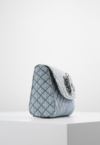 Piccola borsa a tracolla blu chiaro trapuntata con cuciture a rombi nere e un elegante clasp circolare nero, posizionata su un pedestal bianco contro uno sfondo semplice.