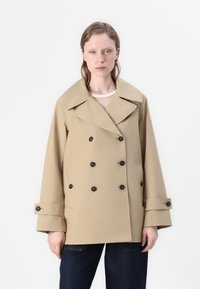 Beige kahepoolne mantel suurte krae ja mustade nuppudega, kahes külg taskus. Vaba lõikega, laiad varrukad ja sile tekstuur.