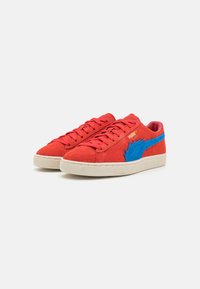 Røde ruskindsneakers med et blåt designelement, gummisål, snørelukning og tekstureret stof. Udstyret med kontrasterende farver og branding.