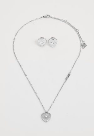 Ezüst szív alakú nyaklánc, rajta egy "GUESS AMORE" feliratú charm, és hozzáillő szív alakú fülbevalók. Mindkettő polírozott felületű.