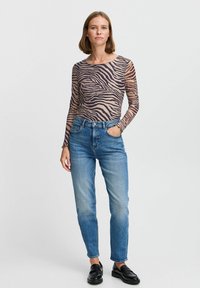 Langærmet top med zebra print mønster, lavet af gennemsigtigt materiale; parret med blå højtaljede skinny jeans og sorte loafers.