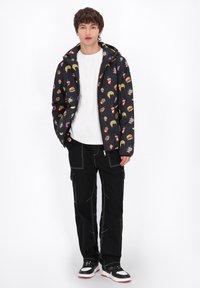 Svart jacka med matteman, vit t-shirt, svarta cargobyxor och svarta sneakers med röda accenter. Texturerad och avslappnad design.
