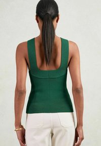 Rippiges grünes ärmelloses Oberteil mit weit ausgeschnittenem quadratischem Rückenausschnitt, taillierter Passform und strukturiertem Stoff, kombiniert mit hellen Hosen.