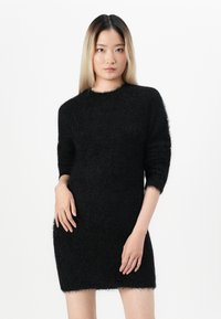 Črna puhasta obleka, izdelana iz teksturiranega materiala. Ima okroglo izrez in trideln sleeves. Ozek kroj z robom tik nad koleni.