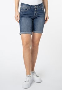 Denimshorts in een donkerblauwe wassing, voorzien van een vijfknops sluiting aan de voorkant, opgerolde mouwen en frontzakken, gecombineerd met witte platform sneakers.