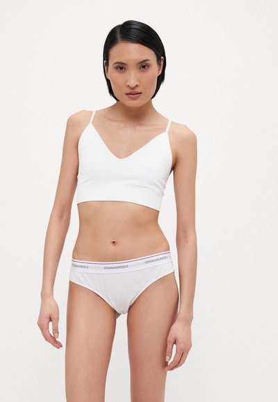 Witte bralette met dunne bandjes en een V-halsontwerp, gecombineerd met witte ondergoed met een merkband in zwart en roze accenten.