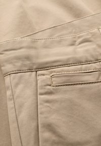 Nahaufnahme von beigem Stoff mit einem genähten Taschendetail an einer Hose.