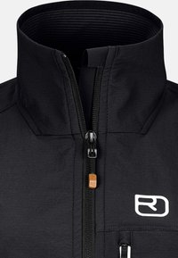 Schwarze Jacke mit hohem Kragen, zentralem Reißverschluss mit dekorativem Ziehfeld und einem Logo im Brustbereich. Glatte Textur, minimalistisches Design.