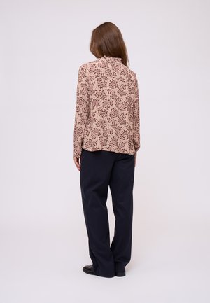 Blusa a maniche lunghe con motivo in crema e bordeaux, abbinata a pantaloni larghi scuri. La blusa presenta un colletto rotondo e una vestibilità rilassata.