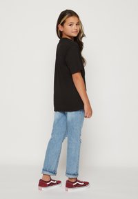 Svart bomullströja, avslappnad passform, tillsammans med ljusblå slitna jeans och vinröda Vans-sneakers med vita accenter.