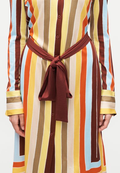 Φόρεμα μακρυμάνικο με κάθετες ρίγες σε κίτρινο, μπεζ, πορτοκαλί, μπλε και καφέ, με κουμπιά μπροστά και δεμένη σκούρα κόκκινη ζώνη στη μέση.