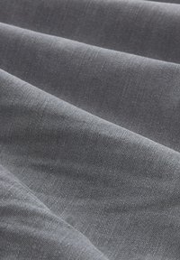 Tessuto denim grigio scuro, caratterizzato da una sottile trama e una superficie leggermente rigata, disposto in pieghe che ne evidenziano la flessibilità.