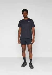 Camiseta atlética preta e calções, feitos de tecido que afasta a humidade. Apresenta um pequeno logótipo branco da Nike. Ténis e meias pretas completam o conjunto.