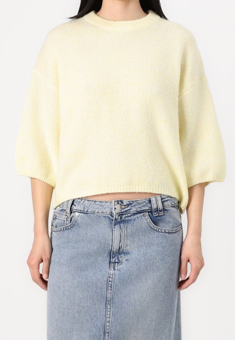 Maglione giallo corto con una vestibilità ampia, colletto a coste e maniche corte, abbinato a una gonna di jeans a vita alta. Tessuto morbido e testurizzato.