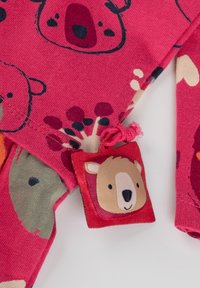 Rosa Baumwolloutfit mit Bärenmotiven in verschiedenen Farben. Enthält ein kleines Stoffetikett mit einem Bärenkopfmuster und einer rosa Kordel.