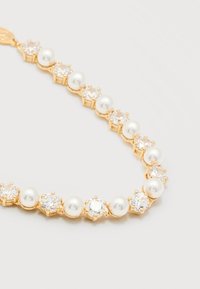 Χρυσό βραχιόλι με εναλλασσόμενες στρογγυλές λευκές πέρλες και διάφανες πολύτιμες πέτρες στερεωμένες σε χρυσά νύχια σε λευκό φόντο.