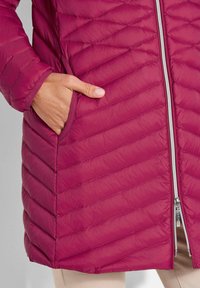 Geverfde magenta pufferjack met een rits aan de voorkant, staande kraag en twee zijzakken. Bevat diagonale stiksels en een gladde textuur.