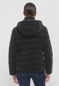 Giacca a vento nera con cappuccio, caratterizzata da pannelli a righe orizzontali, texture morbida, polsini elasticizzati e vestibilità rilassata.