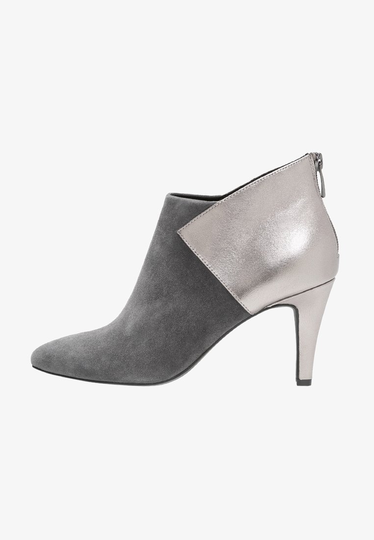 Stivale alla caviglia in suede grigio con punta appuntita, caratterizzato da un accento metallico argentato lucido su un lato e un tacco alto affusolato. Chiusura con cerniera sul retro.