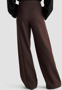 Braune, weit geschnittene Hosen aus glattem Stoff mit hoher Taille und einer dezenten Gesäßtasche, kombiniert mit einem schwarzen Langarmoberteil.