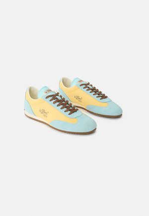 Alacsony szárú sportcipő pár, sárga és világoskék panelekkel, barna fűzőkkel, és "le Fleur" felirattal az oldalán.