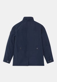 Giacca leggera blu navy con colletto rialzato, due tasche posteriori, chiusure a pressione e una finitura liscia e testurizzata.