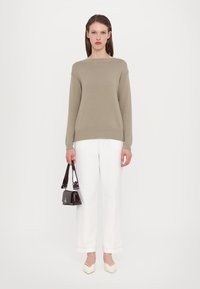 Beige strikkegenser med rund hals, lange ermer, kombinert med hvite vide bukser og en liten svart håndveske. Spisse beige sko.