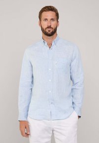 Camicia a scacchi blu chiaro con maniche lunghe, colletto a punta e taschino sul petto. Il tessuto sembra morbido con una superficie liscia.