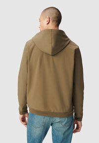 Oliwkowo-zielona kurtka z kapturem o gładkiej fakturze, elastycznych mankietach i dole, zestawiona z jasnoniebieskimi dżinsami. Widok z tyłu ukazuje czyste linie i minimalistyczny design.