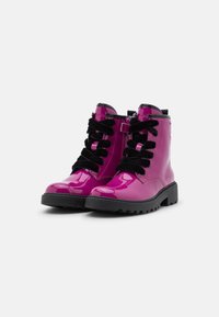 Botas de tobillo de cuero sintético rosa con cordones negros y suela gruesa negra. Cuentan con una cremallera lateral para un fácil acceso.