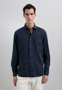 Camisa de manga larga azul marino en un tejido de algodón suave, con botones en la parte delantera, un solo bolsillo en el pecho y un escote relajado.