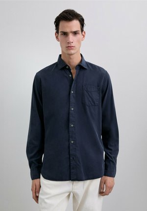 Camisa de manga larga azul marino en un tejido de algodón suave, con botones en la parte delantera, un solo bolsillo en el pecho y un escote relajado.