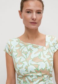 Beiges Blumenkleid mit pastellgrünen und blauen Blattmustern. Es hat einen quadratischen Ausschnitt und kurze Ärmel; aus glattem, leichtem Stoff.