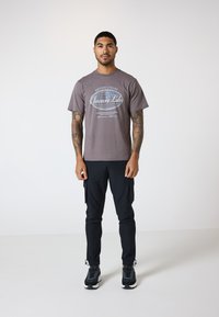Grå bomulds t-shirt med et grafisk logo på forsiden, parret med sorte tapered cargo bukser med sidelommer og elastiske manchetter.