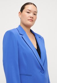 Blazer azul con un diseño estructurado, cierre de un solo botón, solapas muescas y bolsillos laterales. Tejido suave con un acabado mate.
