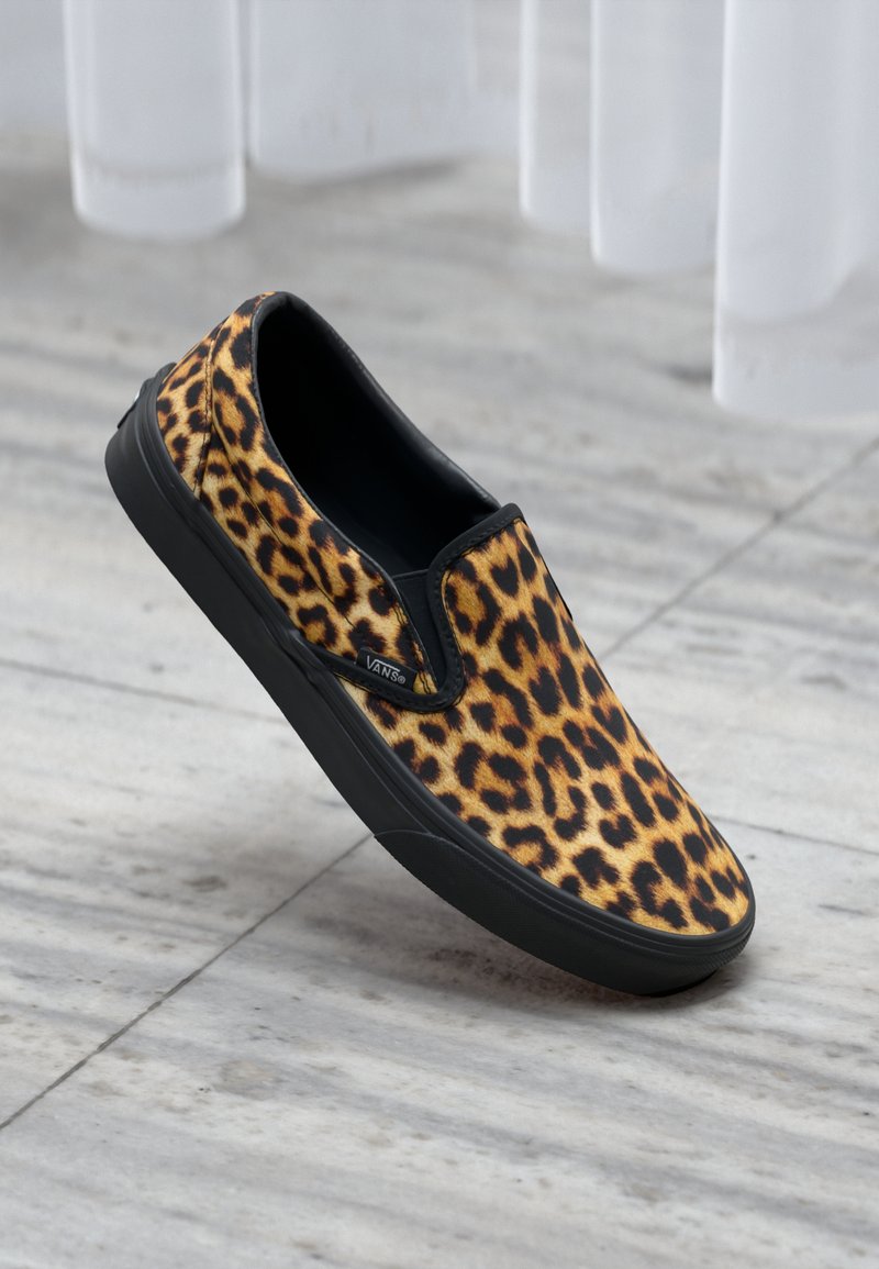 Zapato deslizante de estampado de leopardo hecho de tela con suela de goma negra. Presenta un diseño de perfil bajo y acentos elásticos laterales para un uso fácil.