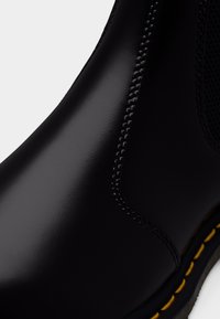 Botte en cuir noir lisse avec une couture détaillée et un fil jaune le long du bord de la semelle.