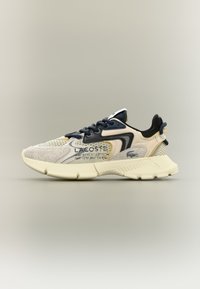 Lacoste'i spordijalats, millel on beez kest ja nubuk, tumesinised aktsendid, tekstureeritud vaheosa ning allkirja bränding külgedel.