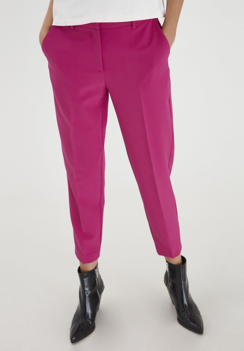 Magenta tailored trousers with side pockets, tapered legs, and a smooth texture, paired with black zippered ankle boots.