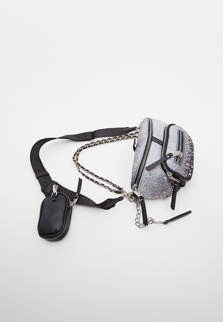 Czarna i srebrna torba crossbody z wieloma zamykanymi kieszeniami, detalami z łańcuszka oraz regulowanym materiałowym paskiem na białym tle.