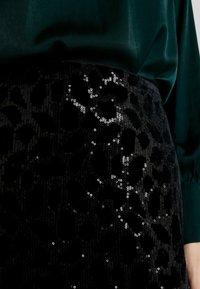 Falda negra de lentejuelas con un patrón de leopardo, tejido texturizado y un acabado brillante. Combinada con una blusa de satén verde oscuro.